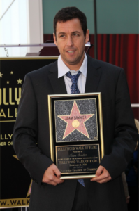 A picture of Adam Sandler holding the Hollywood Walk of Fame award